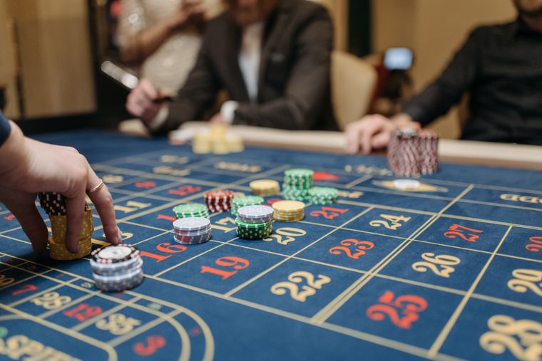 Tangan menempatkan chip di atas meja roulette dengan presisi — simbol membaca syarat dengan cermat